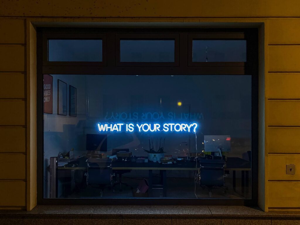 Et vindue, hvor et neonskilt viser teksten what's your story.